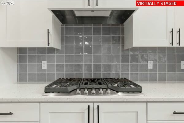10587 SE Webelos Way, Happy Valley, OR 97086 - kitchen featuring under cabinet range hood, white cabinets, stainless steel gas cooktop, backsplash, and light stone countertops