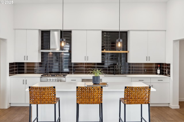 kitchen with hanging light fixtures, a kitchen bar, decorative backsplash, wall chimney exhaust hood, and white cabinetry