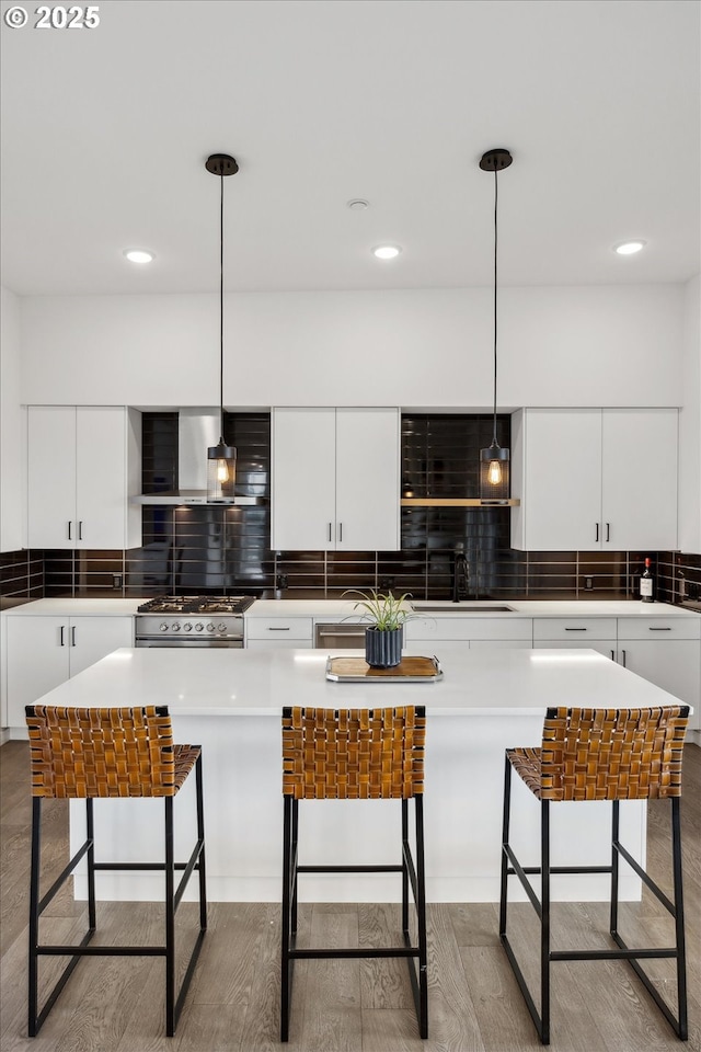 kitchen with a kitchen bar, wall chimney range hood, pendant lighting, and white cabinetry