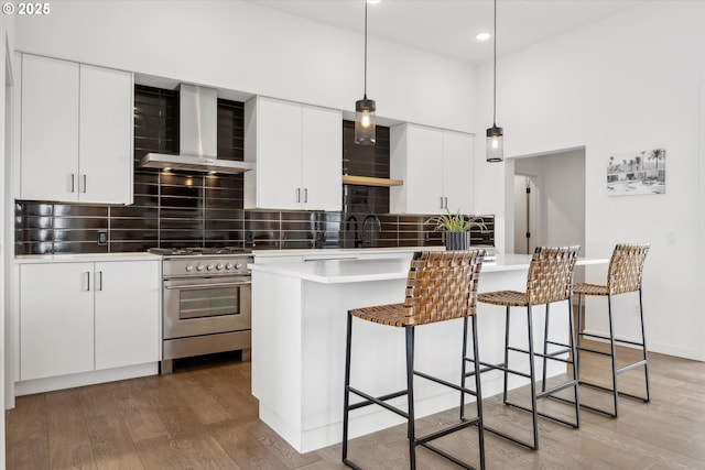 kitchen featuring stainless steel stove, hanging light fixtures, wall chimney range hood, a breakfast bar area, and white cabinets