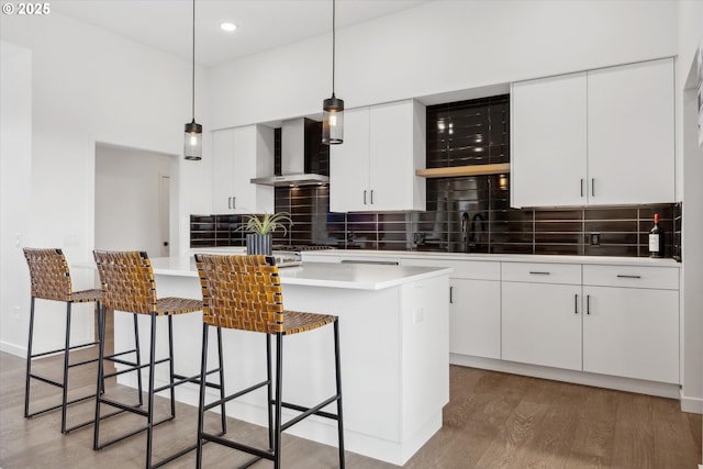 kitchen with pendant lighting, wall chimney exhaust hood, hardwood / wood-style flooring, white cabinetry, and tasteful backsplash