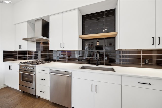 kitchen with wall chimney exhaust hood, decorative backsplash, white cabinets, appliances with stainless steel finishes, and sink