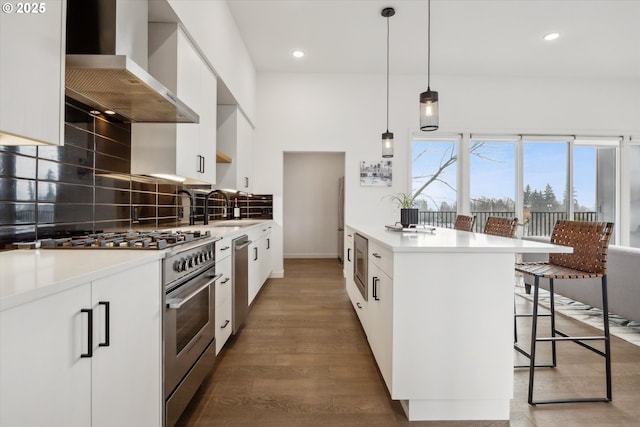 kitchen featuring stainless steel appliances, sink, white cabinetry, hanging light fixtures, and wall chimney range hood