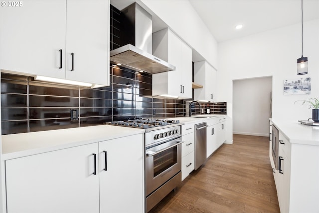 kitchen with appliances with stainless steel finishes, hanging light fixtures, wall chimney range hood, and white cabinets