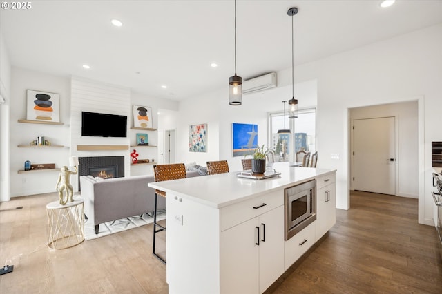 kitchen with white cabinets, a center island, hanging light fixtures, a wall unit AC, and stainless steel microwave