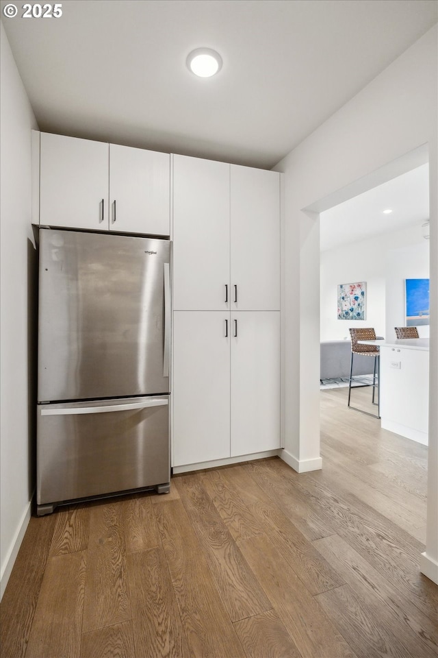 kitchen with stainless steel fridge, light hardwood / wood-style flooring, and white cabinetry