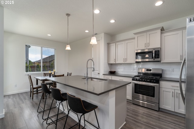 24200 SW Chestnut Ter, Sherwood, OR 97140 - kitchen with stainless steel appliances, dark countertops, tasteful backsplash, a breakfast bar, and a kitchen island with sink