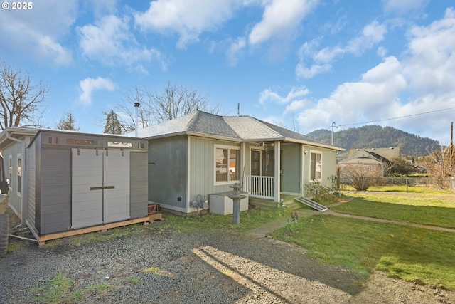 rear view of property featuring a lawn, a storage unit, fence, an outdoor structure, and a mountain view