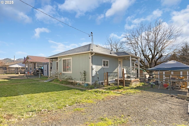 rear view of house featuring a yard, roof with shingles, and fence