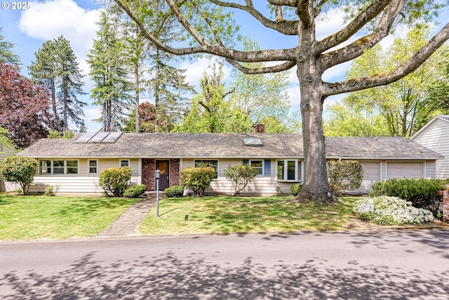 ranch-style home featuring an attached garage, roof mounted solar panels, a front yard, and a chimney