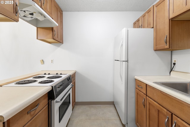 kitchen with a textured ceiling, light countertops, white appliances, and under cabinet range hood