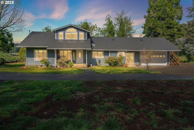 traditional-style home with asphalt driveway, a garage, a porch, a lawn, and roof with shingles