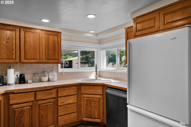 kitchen featuring freestanding refrigerator, dishwasher, a sink, brown cabinets, and backsplash