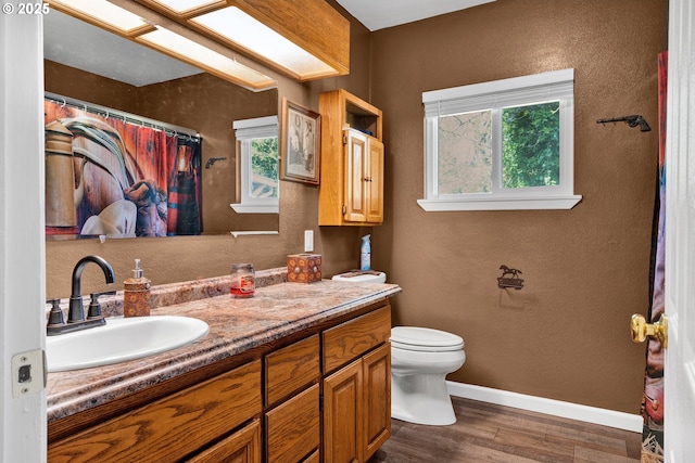 bathroom with wood finished floors, baseboards, a textured wall, healthy amount of natural light, and vanity