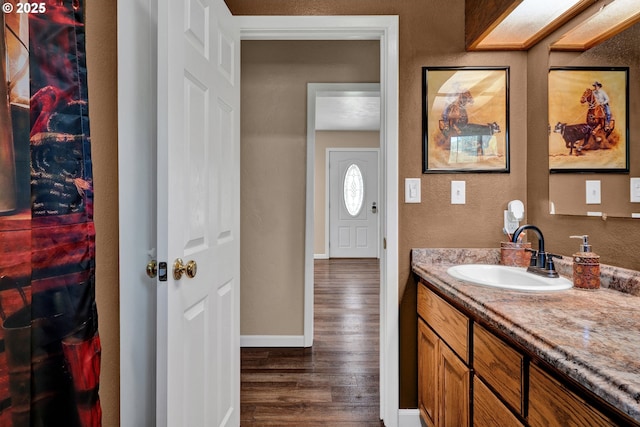 bathroom with wood finished floors, vanity, baseboards, and a textured wall