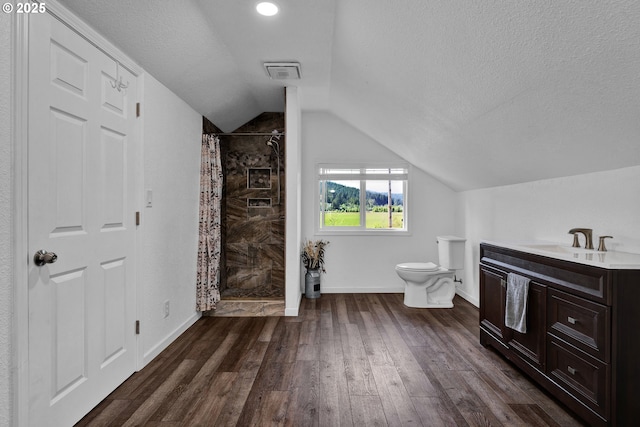 bathroom with toilet, lofted ceiling, a tile shower, wood finished floors, and a textured ceiling