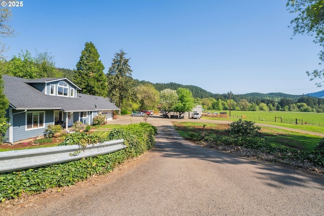 view of asphalt driveway featuring a view of trees and a rural view
