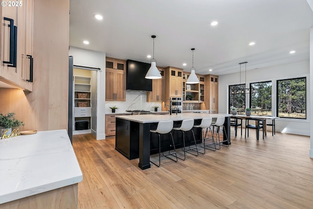 kitchen featuring a breakfast bar area, decorative light fixtures, ventilation hood, light wood-type flooring, and a large island with sink