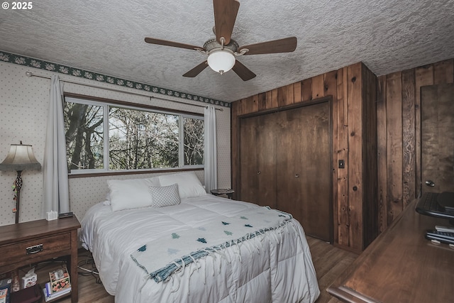 bedroom with a closet, a ceiling fan, a textured ceiling, wood finished floors, and wallpapered walls