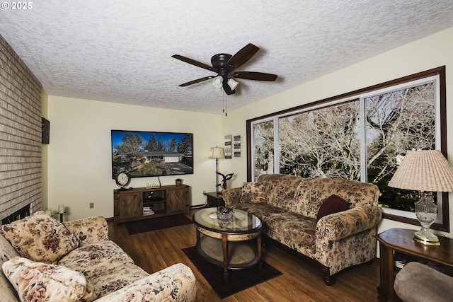 living area with dark wood-style floors, a brick fireplace, a ceiling fan, and a textured ceiling