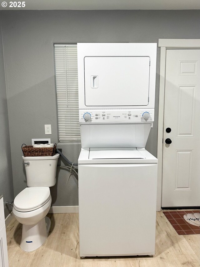 clothes washing area featuring baseboards, stacked washer / drying machine, light wood-style flooring, and laundry area