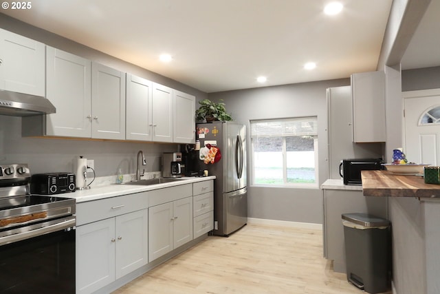 kitchen with appliances with stainless steel finishes, a sink, light wood finished floors, recessed lighting, and baseboards