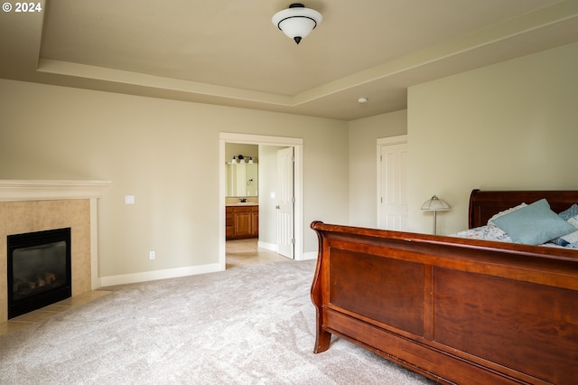 bedroom with a tile fireplace, ensuite bathroom, a tray ceiling, and light colored carpet