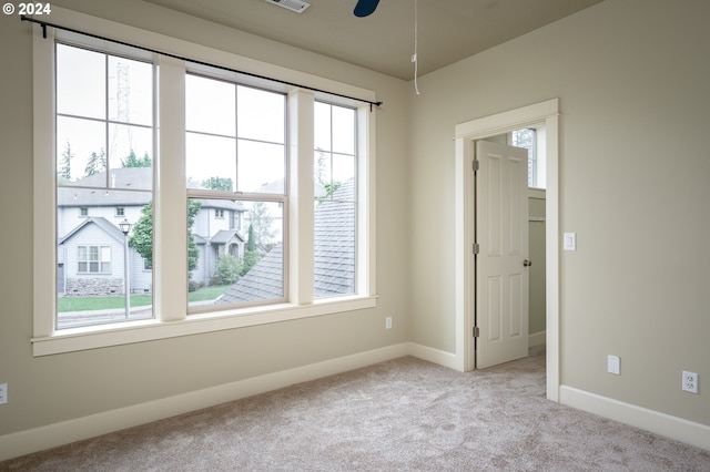 unfurnished room with a wealth of natural light, ceiling fan, and light carpet