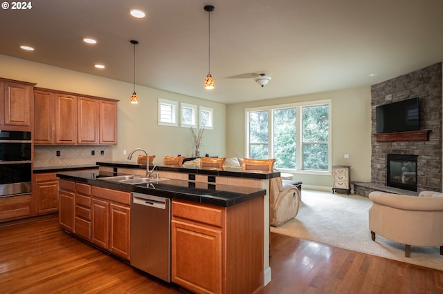 kitchen featuring decorative backsplash, appliances with stainless steel finishes, a kitchen island with sink, sink, and a fireplace