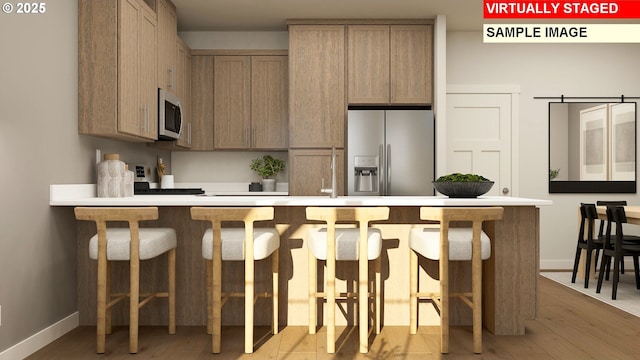 kitchen featuring a breakfast bar area, baseboards, a peninsula, stainless steel appliances, and light countertops