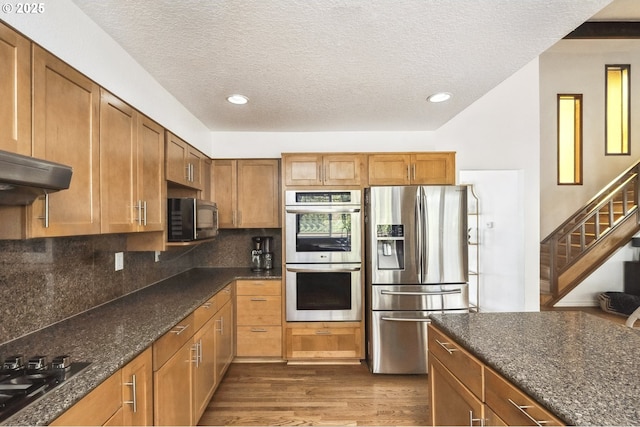 kitchen with dark wood-type flooring, a textured ceiling, dark stone countertops, stainless steel appliances, and backsplash