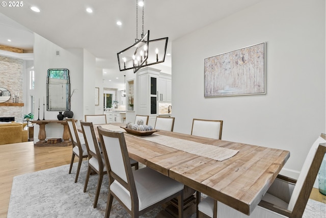 dining space featuring light wood-type flooring, a notable chandelier, and a stone fireplace