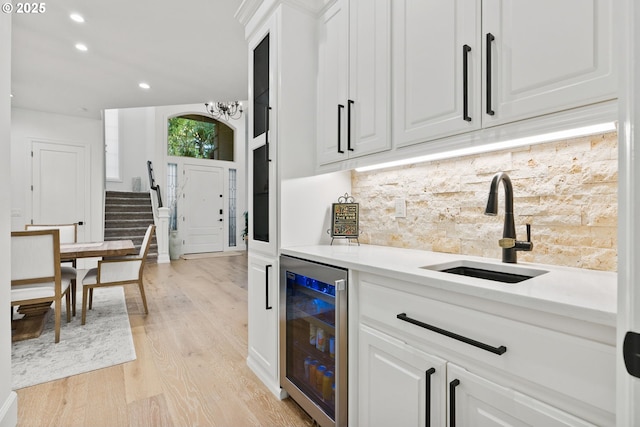 kitchen featuring beverage cooler, light wood-type flooring, sink, white cabinetry, and backsplash