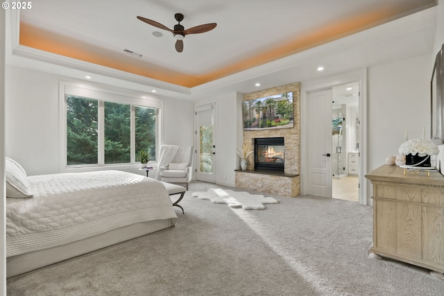 bedroom featuring carpet flooring, a raised ceiling, ceiling fan, ensuite bath, and a stone fireplace