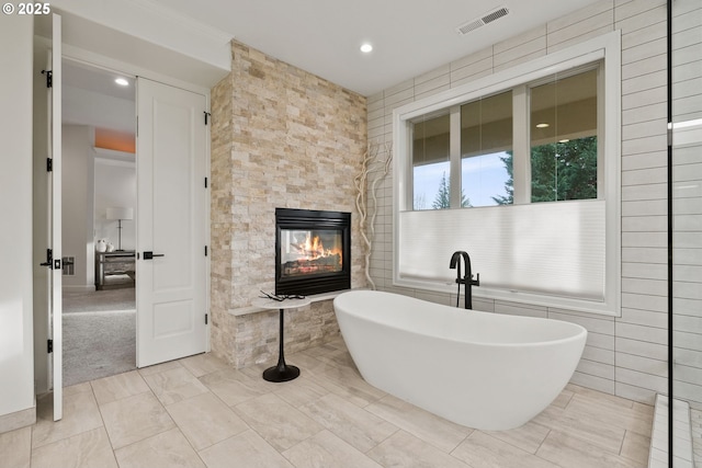 bathroom featuring tile walls, a multi sided fireplace, and a washtub