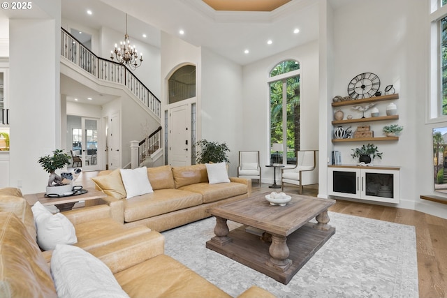 living room with light wood-type flooring, an inviting chandelier, a towering ceiling, and plenty of natural light