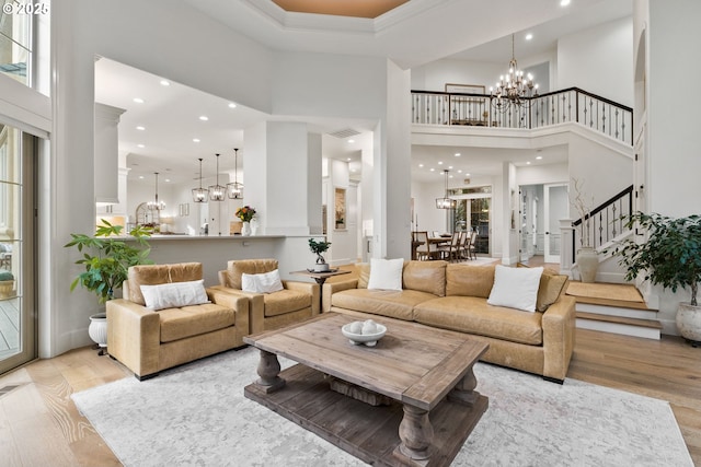 living room with a high ceiling, light wood-type flooring, a healthy amount of sunlight, and a notable chandelier