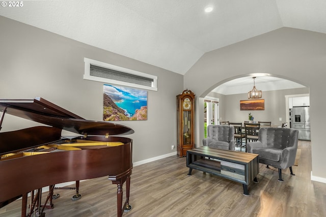 living area with arched walkways, vaulted ceiling, baseboards, and wood finished floors