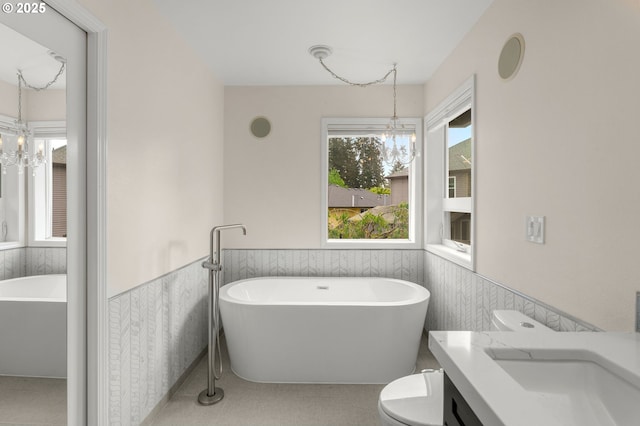 full bath featuring a chandelier, a freestanding tub, a wainscoted wall, vanity, and toilet