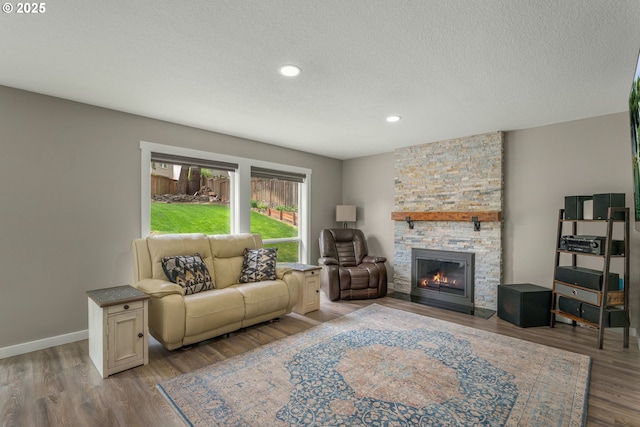 living area with a stone fireplace, a textured ceiling, wood finished floors, recessed lighting, and baseboards