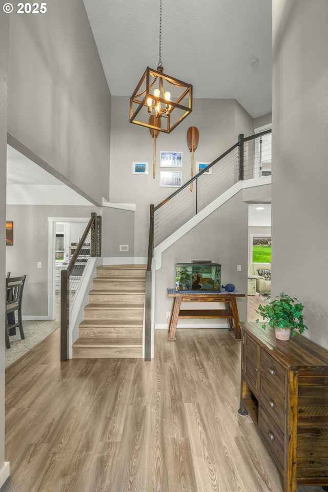 entryway featuring a high ceiling, stairs, a chandelier, wood finished floors, and baseboards