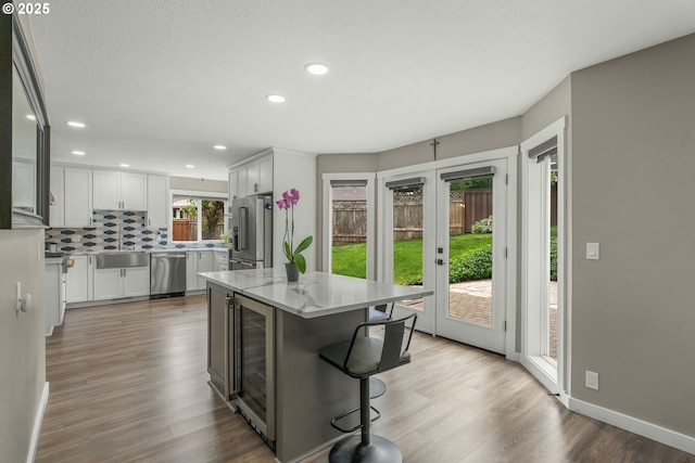 kitchen with stainless steel appliances, a sink, wood finished floors, white cabinetry, and backsplash
