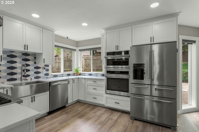 kitchen with appliances with stainless steel finishes, white cabinetry, decorative backsplash, a sink, and recessed lighting