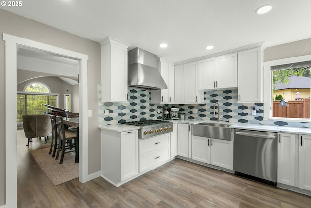 kitchen with stainless steel appliances, wall chimney exhaust hood, light countertops, a sink, and wood finished floors