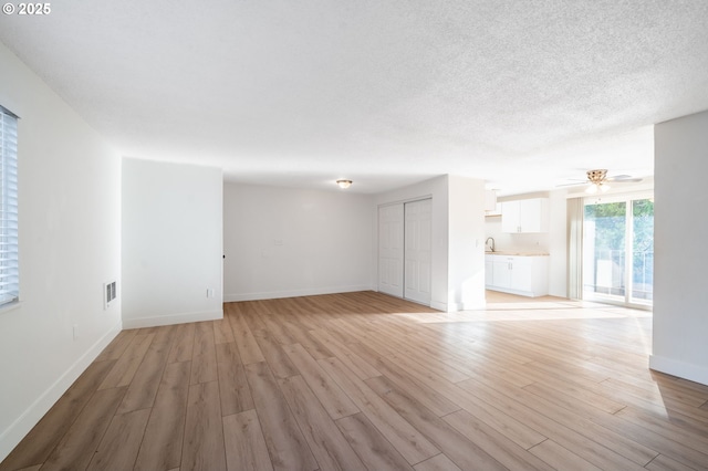 unfurnished living room featuring light wood-style flooring, a textured ceiling, baseboards, and a sink