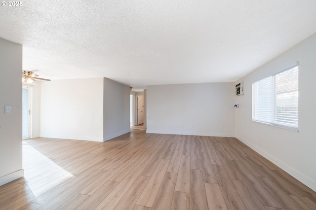 spare room with a ceiling fan, baseboards, an AC wall unit, light wood-style floors, and a textured ceiling