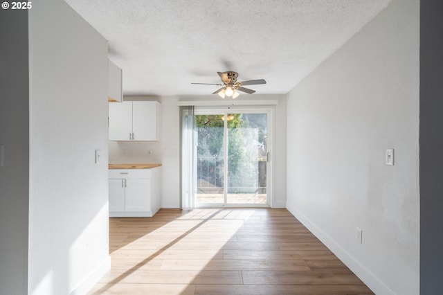 interior space featuring baseboards, ceiling fan, a textured ceiling, white cabinetry, and light wood-type flooring