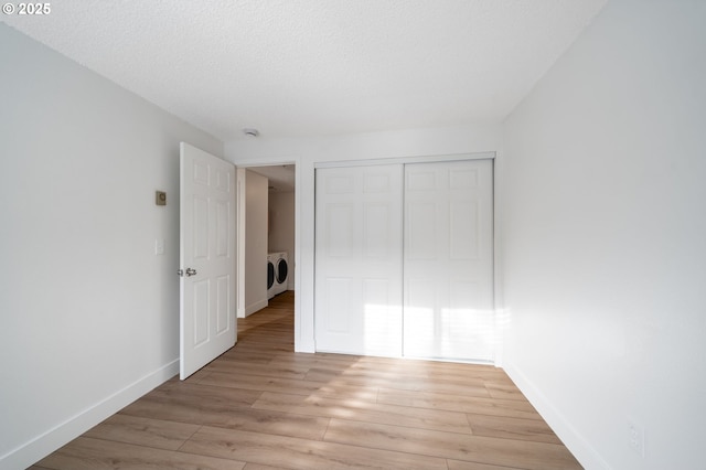 unfurnished bedroom with baseboards, light wood-style floors, a closet, independent washer and dryer, and a textured ceiling