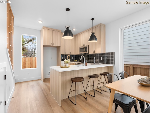 kitchen featuring light brown cabinets, a peninsula, light countertops, stainless steel microwave, and light wood-type flooring