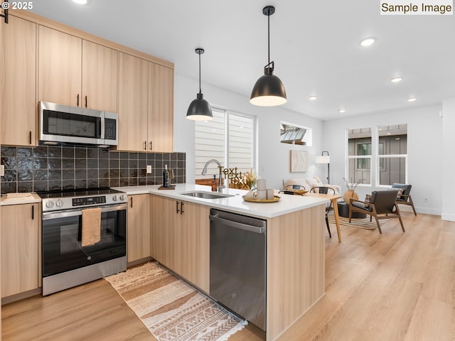 kitchen with light brown cabinets, a peninsula, a sink, stainless steel appliances, and light wood-style floors